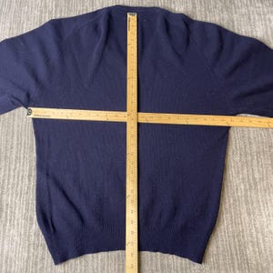 Puede incluir: Un su&eacute;ter azul marino de manga larga con dobladillo y pu&ntilde;os acanalados. Una regla de madera est&aacute; colocada vertical y horizontalmente sobre la prenda, mostrando un ancho de aproximadamente 58,4 cm y un largo de aproximadamente 71,1 cm.