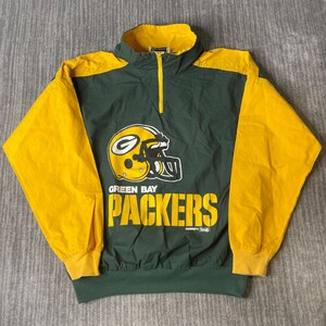 May include: A dark green and yellow pullover windbreaker jacket featuring a half-zip collar and long sleeves. The front displays a yellow football helmet graphic with a green G logo and the text GREEN BAY PACKERS in bold yellow lettering.
