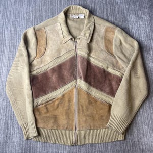 May include: A full-zip jacket featuring a combination of beige ribbed knit sleeves and collar with panels of tan, brown, and dark brown suede leather. The front includes a chevron-patterned suede design accented with a cable knit texture.