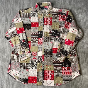May include: A long-sleeve button-down shirt featuring a patchwork design with various geometric, paisley, and floral patterns in shades of red, olive green, black, white, and gray. The shirt has a standard collar, a front button placket, and cuffs.