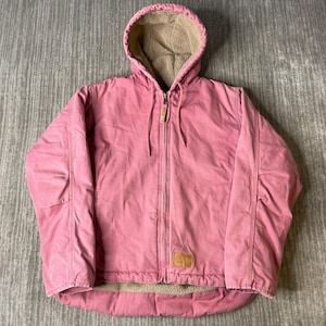 May include: A dusty rose hooded jacket featuring a full-length front zipper with a metal pull, long sleeves, and a tan sherpa-style fleece lining. The exterior is made of a heavy-duty fabric, and a small rectangular tan patch is visible at the bottom.