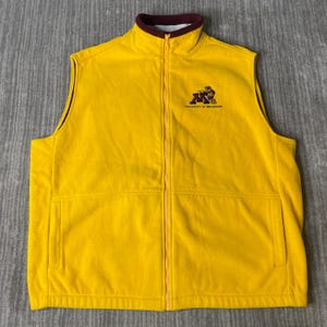 May include: A yellow fleece vest with a full-length zip and a stand-up collar. The vest has a maroon trim on the collar and armholes. The University of Minnesota logo is embroidered on the chest.