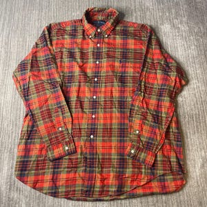 May include: A long-sleeve button-down shirt featuring a plaid pattern in shades of red, green, yellow, and navy blue. The shirt has a button-down collar, a front button placket, and a small embroidered logo on the left chest area of the garment.