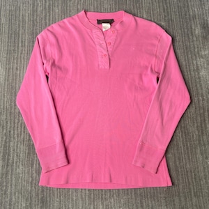 May include: A long-sleeved, bright pink shirt with a Henley neckline. The shirt features a ribbed cuff at the wrist and a three-button placket. The fabric appears to be a soft, knit material.