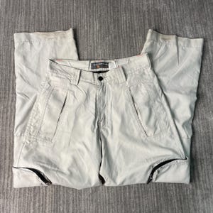 May include: Light gray cropped pants with a button closure and zipper pockets. The pants have a straight leg design and feature black zippers at the ankles. The brand name "SILVERTAB" is visible on the label.