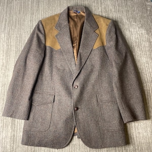 May include: A brown tweed blazer with tan suede shoulder patches. The blazer has two front pockets and a two-button closure. The interior lining is a light brown color.