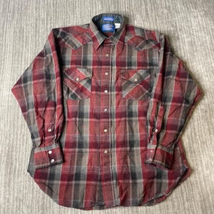 Op de afbeelding: Een button-down shirt met lange mouwen in een ruitpatroon van rood, grijs en zwart. De shirt heeft twee borstzakken met knoopsluitingen en een kraag met een klein label. De shirt is gemaakt van een zachte, geweven stof.