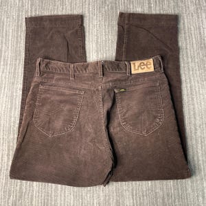 May include: Brown corduroy pants with the Lee logo on the back pocket. The pants have a classic five-pocket design and a straight leg. The corduroy fabric has a vertical ribbed texture.