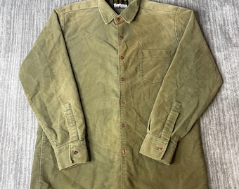 May include: An olive green long-sleeve corduroy shirt featuring a button-down front, a pointed collar, and a single chest pocket. The shirt includes a Barbour brand label on the inner collar and matching buttons along the placket and cuffs.