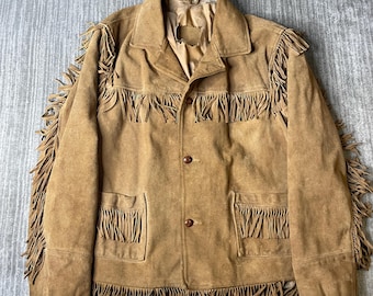 Peut inclure: Une veste en daim beige avec de longues franges sur les manches, la poitrine et l'ourlet. La veste présente un col pointu, deux poches avant ornées de franges et trois boutons marron sur la fermeture centrale à l'avant.