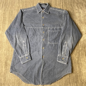 May include: A long-sleeve button-down shirt in a muted blue-grey corduroy fabric. The shirt features a standard collar, a single chest pocket on the left side, and light-colored buttons running down the front placket and on the sleeve cuffs.