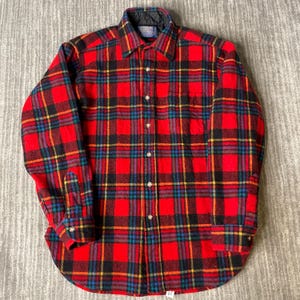 May include: A long-sleeve button-up shirt featuring a vibrant red, black, yellow, and blue plaid pattern. The shirt has a classic collar, a front button placket, and a single chest pocket. The interior collar lining is black and quilted.