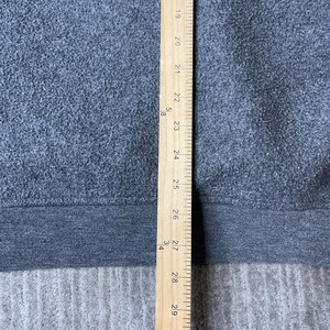 May include: A gray fabric with a dark gray band at the bottom, measured with a wooden ruler. The ruler shows measurements from 19 to 29 inches. The fabric appears to be a sweatshirt or similar garment.
