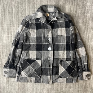 May include: A long-sleeve button-down jacket featuring a black, charcoal, and light gray plaid pattern. The jacket includes a pointed collar, four front buttons, two square patch pockets at the waist, and buttoned cuffs on each sleeve.