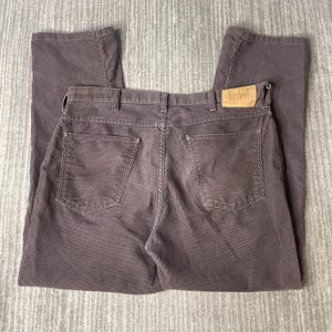 Puede incluir: Pantalones de pana en un tono marrón apagado. Los pantalones tienen un diseño clásico de cinco bolsillos con corte recto. Una etiqueta de cuero con el texto "PLAID JOCKERS" es visible en la parte trasera. La tela de pana tiene estrías verticales.