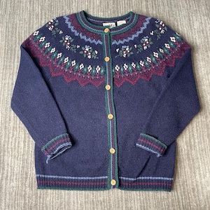 May include: A navy blue cardigan sweater with a floral pattern across the yoke and cuffs. The sweater has a round neckline, wooden buttons, and trim in green, red, and blue. The cuffs and hem have striped detailing.