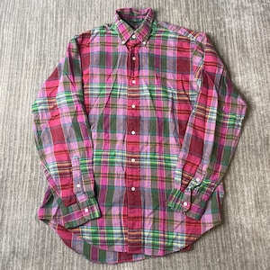 May include: A long-sleeve button-down shirt featuring a vibrant plaid pattern in shades of magenta, dark red, green, and yellow. The shirt has a classic collar, a front button placket, and buttoned cuffs, with a small embroidered logo on the chest.