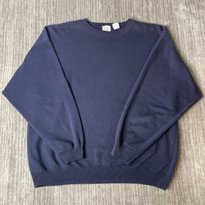 Könnte beinhalten: Ein einfarbiges, marineblaues Langarm-Sweatshirt mit Rundhalsausschnitt, geripptem Kragen, Bündchen und Saum. Das Kleidungsstück verfügt über ein kleines weißes Markenetikett am inneren Halsausschnitt mit dem in Schwarz gedruckten Text GAP.