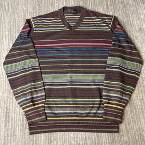 May include: A brown V-neck sweater with horizontal stripes in various colors, including blue, pink, and green. The sweater has long sleeves and a ribbed hem and cuffs. The brand name is visible on the upper chest.