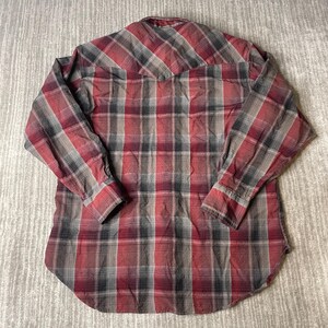 Op de afbeelding: Een rood, zwart en grijs geruit shirt met lange mouwen. Het shirt heeft een knoopsluiting, een puntkraag en manchetten met knopen. De stof heeft een licht versleten uiterlijk.