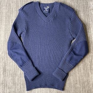 May include: A navy blue V-neck sweater featuring a ribbed knit texture, long sleeves with solid fabric elbow patches, and matching shoulder epaulets. The interior neck label displays the brand name Citadel with additional garment care text.