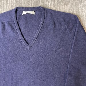 Puede incluir: Un su&eacute;ter azul marino con cuello en V, mangas largas y escote acanalado. La prenda presenta una etiqueta interior blanca en el cuello que dice Pringle of Scotland y menciona cachemira. El tejido de punto tiene una textura consistente.