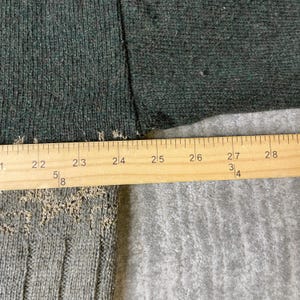 K&ouml;nnte beinhalten: Nahaufnahme eines dunkelgr&uuml;nen Stoffes mit einem Holzlineal. Das Lineal zeigt Messungen von 53 cm bis 71 cm. Der Stoff hat eine strukturierte Optik.