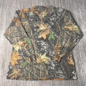 May include: Long-sleeved camouflage shirt featuring a pattern of brown, green, and tan leaves and branches. The shirt has a crew neck and long sleeves, suitable for outdoor activities or casual wear. The fabric appears to be a blend, offering comfort and durability.