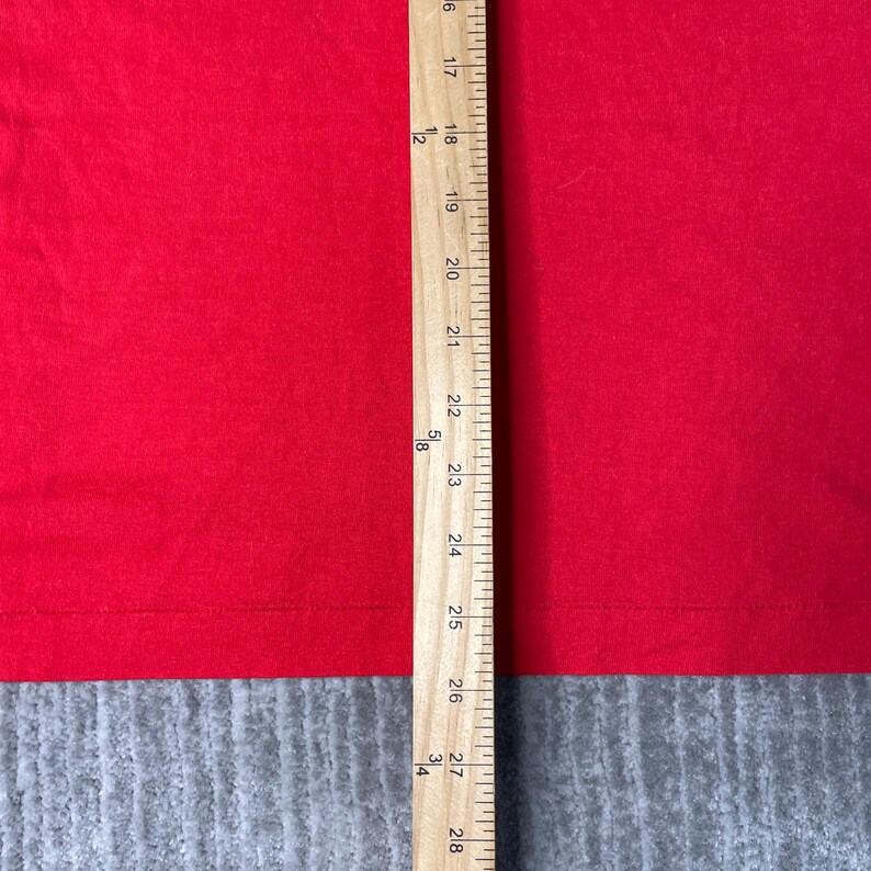 May include: A close-up of red fabric with a wooden ruler placed vertically. The ruler shows measurements from 16 to 28 inches. The fabric is a solid, vibrant red colour.
