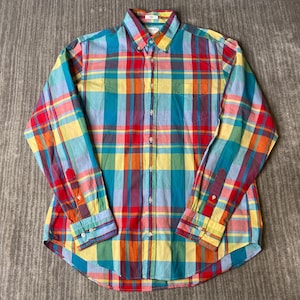 May include: A long-sleeved button-down shirt with a colorful plaid pattern. The shirt features a classic collar, a chest pocket, and buttoned cuffs. The plaid design incorporates red, yellow, blue, green, and orange hues.