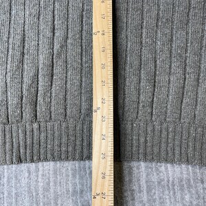 K&ouml;nnte beinhalten: Nahaufnahme eines grauen Rippstrickstoffs mit einem Holzlineal an der rechten Seite. Das Lineal zeigt Messungen in Zoll, von 16 bis 27 Zoll (ca. 40,6 bis 68,6 cm). Der Stoff hat vertikale Rippen.