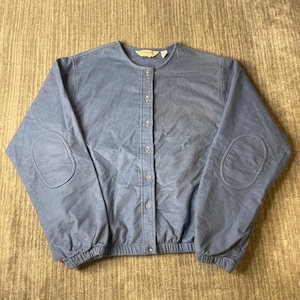 May include: A dusty blue long-sleeve cardigan featuring a crew neckline, a front button-down closure with matching buttons, and reinforced oval elbow patches on each sleeve. The garment has an elasticized hem and cuffs for a gathered fit.