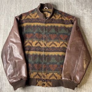 May include: A varsity-style jacket featuring brown leather sleeves and a wool-blend body with a multi-coloured geometric pattern in shades of mustard yellow, forest green, and dark brown. It includes a ribbed brown collar, cuffs, and hem with snap buttons.
