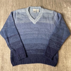May include: A long-sleeve V-neck sweater featuring a horizontal ombre gradient pattern that transitions from light blue at the neckline to a deep navy blue at the hem. The knit garment includes a ribbed collar, cuffs, and hem with a JALATE brand label.
