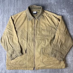 May include: A tan zip-up jacket featuring a corduroy collar, a full-length front zipper, and multiple pockets. The garment includes a chest pocket with a flap and two lower patch pockets. A black DKNY brand label is visible on the inner collar.