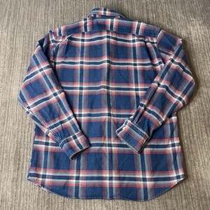 May include: A long-sleeved, button-down shirt in a classic plaid pattern. The shirt features a navy blue base with red and white intersecting lines, creating a traditional checkered design. The cuffs and collar are visible, and the shirt is laid flat.