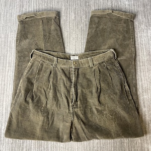 May include: Olive green corduroy trousers featuring a high-waisted design with double front pleats, a button and zipper fly closure, belt loops, and cuffed hems. A white label with the text "SCOLE BOY Original" is sewn inside the waistband.