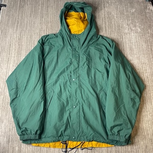 May include: A forest green hooded jacket featuring a mustard yellow interior lining. The jacket has a front placket with snap button closures, long sleeves with elastic cuffs, and a drawstring hem at the bottom. The hood is attached and fixed.