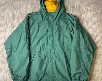 May include: A forest green hooded jacket featuring a mustard yellow interior lining. The jacket has a front placket with snap button closures, long sleeves with elastic cuffs, and a drawstring hem at the bottom. The hood is attached and fixed.