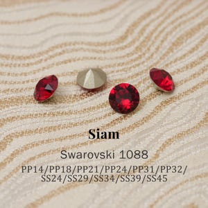 Puede incluir: Primer plano de varios cristales Swarovski Siam rojos. Los cristales tienen varias formas, incluyendo redonda y ovalada. El texto "Siam" y "Swarovski 1088" son visibles, junto con códigos de tamaño.