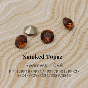 Op de afbeelding: Close-up van verschillende Smoked Topaz Swarovski kristallen. De kristallen hebben verschillende vormen, waaronder rond en ovaal, en een warme, bruine kleur. De tekst "Smoked Topaz" en "Swarovski 1088" zijn zichtbaar.