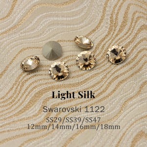 May include: A collection of Light Silk Swarovski crystals in various shapes and sizes, including round and oval cuts. The image displays the text "Light Silk", "Swarovski 1122", and size details: 12mm, 14mm, 16mm, and 18mm.