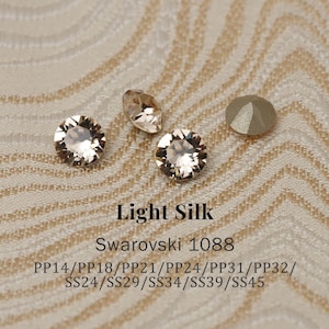 May include: Close-up of several Light Silk Swarovski crystals in various shapes. The crystals are a light beige color and reflect light. Text on the image reads "Light Silk" and "Swarovski 1088", along with size codes.