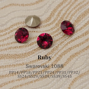 May include: Close-up of several ruby-colored Swarovski crystals and one silver-colored crystal. The text "Ruby" and "Swarovski 1088" are visible, along with size codes. These faceted gemstones are ideal for jewelry making and crafts.