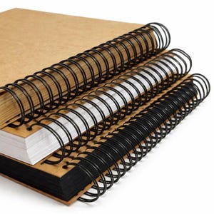 May include: A stack of three spiral-bound notebooks with tan cardboard covers. The top notebook has tan pages, the middle notebook has white pages, and the bottom notebook has black pages. Each notebook features a black metal wire coil.