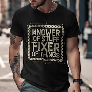 Può includere: T-shirt nero con un design invecchiato con la scritta "Knower of Stuff, Fixer of Things" in una cornice a catena. La maglietta è indossata da una persona con tatuaggi sul braccio.