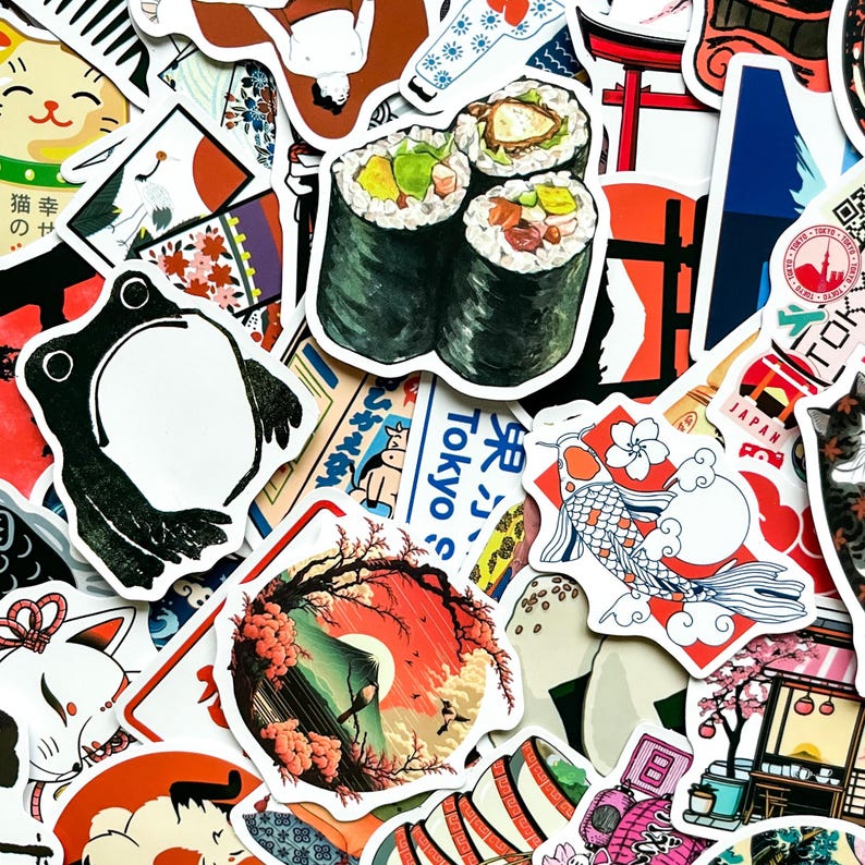 May include: A collection of colorful Japanese-themed stickers. The stickers feature sushi rolls, a frog, a koi fish, a cat, and a landscape with a mountain and cherry blossoms. Some stickers have Japanese text.