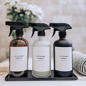 Puede incluir: Tres botellas de spray de vidrio con boquillas negras y etiquetas blancas que dicen "KITCHEN SPRAY". Las botellas son marrones, esmeriladas y negras, y están sobre una bandeja negra. Cada botella contiene 500 ml.