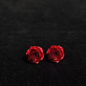 May include: Two vibrant red rose buds, captured in a close-up shot against a dark, textured background. The roses are in full bloom, showcasing their intricate petal arrangement. The image highlights the natural beauty of the flowers.
