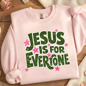 May include: A light pink sweatshirt with the text "JESUS IS FOR EVERYONE" in green, outlined in white, and decorated with pink stars. The sweatshirt has long sleeves and a crew neck.